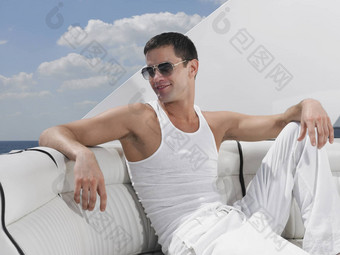 英俊的年轻的男人。穿太阳镜放松沙发奢侈品游艇