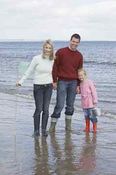 肖像快乐父母女儿持有钓鱼网桶海滩