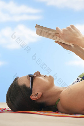 一边视图年轻的女人穿太阳镜阅读<strong>书海</strong>滩
