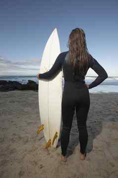 完整的长度后视图年轻的女人冲浪板站海滩