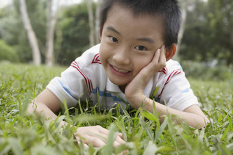 特写镜头肖像快乐的年轻的男孩说谎草公园