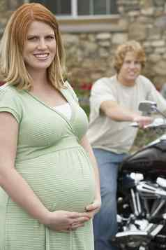 肖像快乐怀孕了女人站男人。摩托车背景