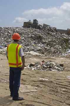 工人看挖掘机移动浪费垃圾填埋场网站