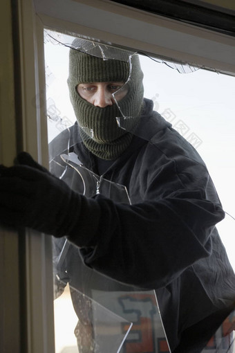 戴面具的小偷打破房子窗口