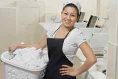 肖像快乐年轻的女员工携带洗衣篮子自助洗衣店