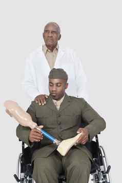 高级医生军事官持有人工肢体坐在轮椅灰色的背景