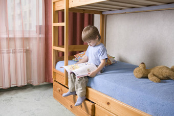一年男孩坐在双层床上阅读书