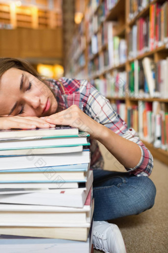 打瞌睡年轻的学生坐着图书馆地板上倾斜桩书