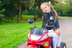 可爱的可爱的女孩皮革夹克坐着玩具摩托车