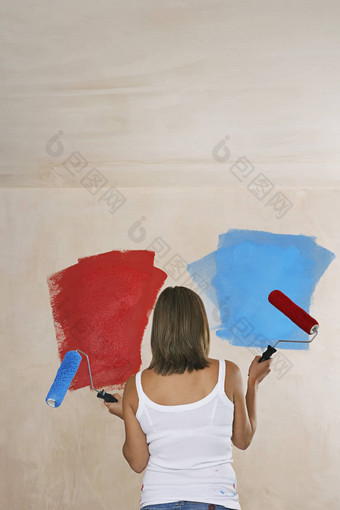 女人面对墙画是红色的持有油漆辊回来视图