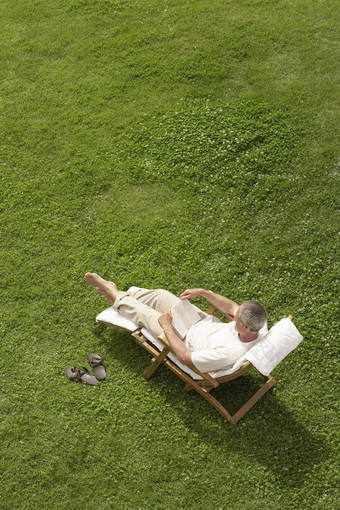 中年男人。倾斜的草坪上甲板椅子阅读高角视图