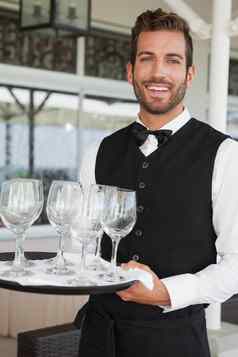 英俊的服务员持有托盘葡萄酒杯