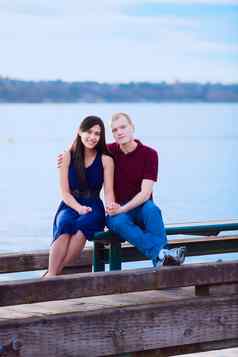 年轻的跨种族夫妇坐着码头湖