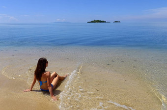 年轻的女人比基尼坐着海滩瓦莱武岛,使