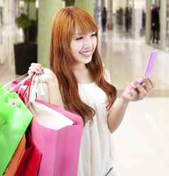 年轻的女人持有移动电话购物袋购物中心