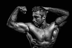 英俊的肌肉发达的健美运动员摆姿势黑色的背景