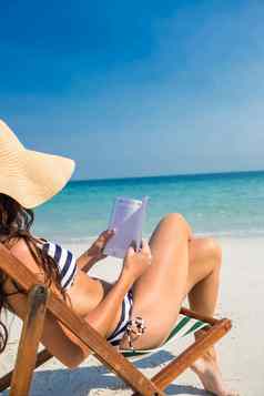 漂亮的浅黑肤色的女人阅读甲板椅子海滩
