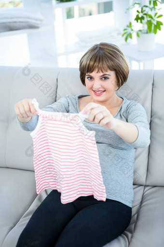 肖像微笑怀孕了女人持有婴儿衣服