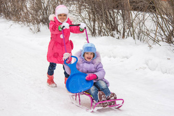 老女孩卷年轻的女孩雪橇院子里