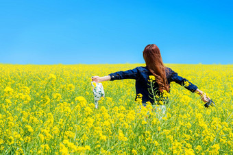 年轻的女人站黄色的油菜籽场