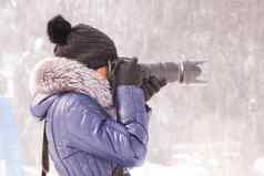 年轻的女孩拍摄冬天雪风暴单反相机长焦镜头