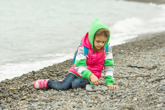七年女孩坐着卵石海滩温暖的服装热情戏剧石头