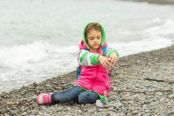 七年女孩坐着卵石海滩温暖的服装倒手指小石头