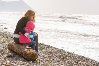 妈妈。一年女儿坐着海滩妈妈。拥抱冻女孩
