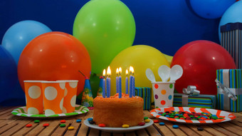 生日蛋糕蓝色的蜡烛燃烧乡村木表格背景色彩斑斓的气球礼物塑料杯塑料板糖果蓝色的墙背景