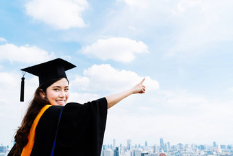 美丽的亚洲大学大学研究生学生女人毕业学术衣服礼服微笑指出复制空间蓝色的天空背景教育成功概念