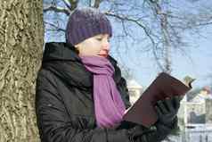 年轻的夫人阅读书在户外冬天时间