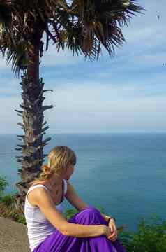 年轻的女人坐着海滨棕榈看海边