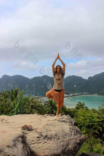 年轻的男人。站莲花瑜伽构成岩石在户外斐不岛泰国湾视图