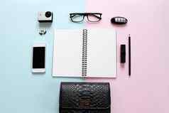 工作空间桌子上空白笔记本铅笔口红车关键眼睛眼镜小行动相机耳环袋聪明的电话粉红色的蓝色的背景
