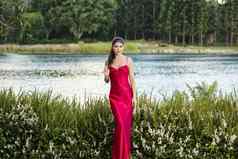美丽的年轻的女人花园穿长丝绸红色的衣服