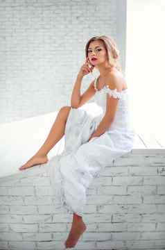 美丽的女孩白色衣服梦想坐着砖墙