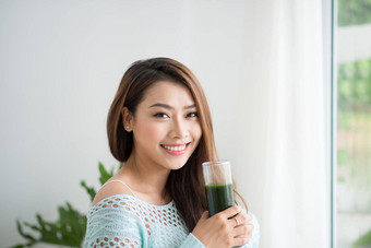微笑年轻的亚洲女人喝绿色新鲜的<strong>蔬菜汁</strong>