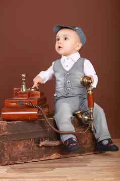 可爱的婴儿坐着手提箱持有古董电话