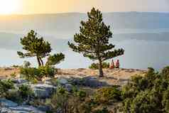 成熟的夫妇坐着大岩石俯瞰海滨日落地平线