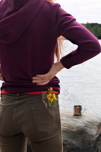 英俊的女旅游穿棕色（的）牛仔裤紫色的运动衫叉黄色的花口袋里站河银行享受视图山夏天徒步旅行旅行概念垂直