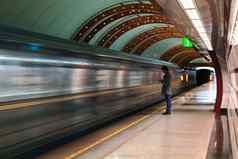 孤独的年轻的男人。智能手机拍摄配置文件地铁站模糊的移动火车背景