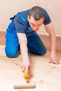 熟练的年轻的工人油漆辊木地板上房子