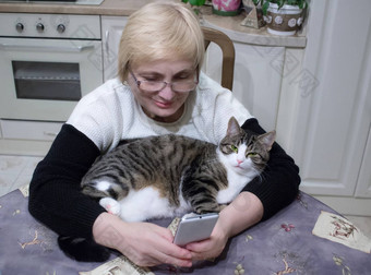 上了年纪的女人<strong>手表电话</strong>坐着厨房表格猫