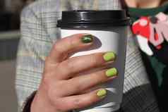 美丽的女手修指甲持有纸板咖啡杯温柔的黄色的指甲波兰的绿色猫眼睛设计