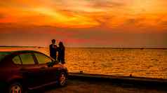 轮廓幸福夫妇站车海边日落美丽的橙色天空云路旅行
