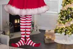 可爱的圣诞节精灵女孩穿条纹长袜站装饰圣诞节生活房间礼物圣诞节树背景
