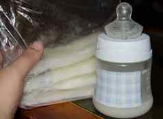 女人手持有冻乳房牛奶存储袋婴儿瓶新鲜的expresed母乳