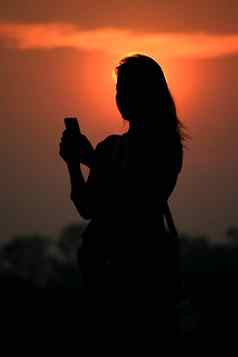 轮廓亚洲女人触碰智能手机日落时间