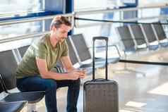 乘客机场休息室等待飞行飞机年轻的男人。手机机场等待着陆