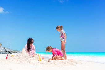 家庭使沙子城堡热带白色海滩妈妈。女孩玩沙子热带海滩
